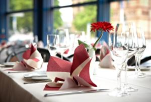 a table with wine glasses and a red flower on it at IntercityHotel Schwerin in Schwerin