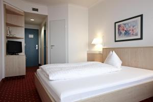 a bedroom with a large white bed and a tv at IntercityHotel Schwerin in Schwerin