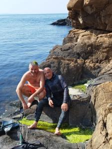 two men sitting on a rock near the water at АПАРТАМЕНТ АРГАНТОНЕ in Sinemorets