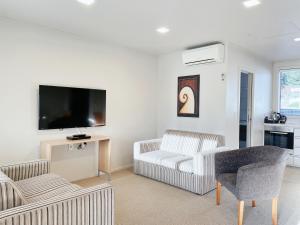 a living room with two chairs and a flat screen tv at Anchorage Motel Apartments in Te Anau