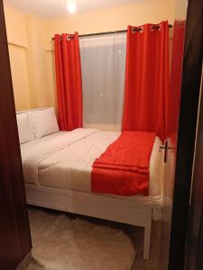 Una pequeña cama con cortinas rojas y una ventana. en J's Haven, en Kisumu