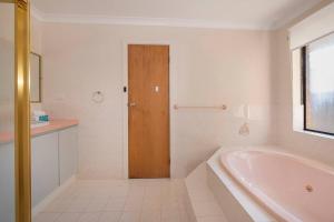 a white bathroom with a tub and a wooden door at Duke Street Hideaway in Busselton +5 photos