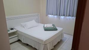 a white bed with a purse on top of it at Rivello Apart Hotel in Sete Lagoas