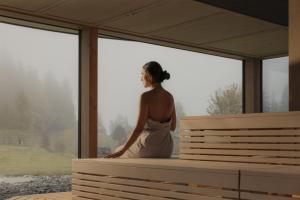a woman sitting on a bench looking out the window at Berghotel Schlossanger Alp in Pfronten