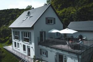 una casa bianca con un balcone con persone sedute sotto un ombrellone di Freistehendes Ferienhaus mit Kamin, Sauna, atemberaubenden Blick ins Tal, mehrere Terrassen, 1500qm Grundstück 1,6m hoch eingezäunt a Gerabronn