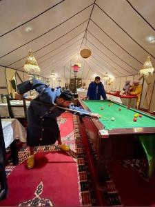 Un hombre está blandiendo un taco de billar. en TRIP Merzouga luxury camp, en Adrouine