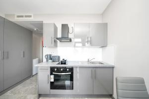 a white kitchen with a sink and a stove at Studio with Balcony Godino Hotel Ilford in Ilford +2 photos