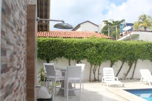 a patio with white chairs and a table and a hedge at Casa Luxuosa - Porto de Galinhas in Porto De Galinhas