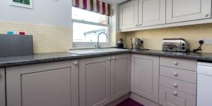 eine Küche mit weißen Schränken und einer Spüle und einem Fenster in der Unterkunft Waterfront Cottage in Aldeburgh