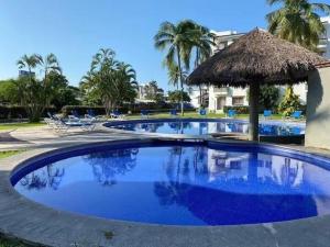 a large swimming pool with a thatch roof at Precioso depa a 70 mts de playa in Manzanillo