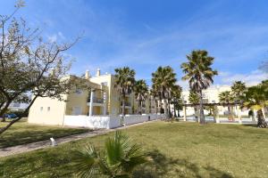 a large white building with palm trees in a park at Praia da Lota Beachfront Resort - Hotel & Apartments in Manta Rota