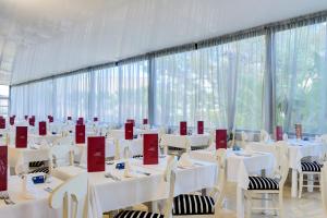 a room with white tables and chairs and large windows at Cala Millor Garden Hotel - Adults Only in Cala Millor