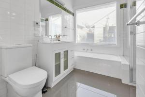 a white bathroom with a toilet and a tub and a window at Cottswold in Paynesville +19 photos