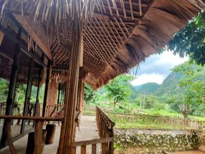 un bâtiment avec un toit en bambou avec des montagnes en arrière-plan dans l'établissement Hải Nam Homestay Hòa Bình, à Mai Châu