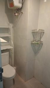 a white bathroom with a toilet and a shelf at FREE WIFI, NETFLIX, SMART TV, MINERAL WATER, AMENITIES - Studio with Foldable Wall Bed at Serpong Garden Apt in Cisauk 1 +6 photos