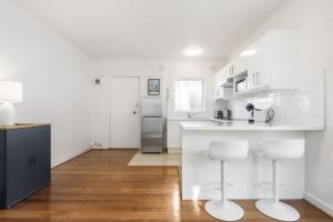 a white kitchen with a counter and two stools at Seaside 1-Bed Stay Near Cafés & Attractions in Melbourne