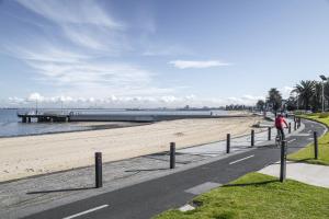 a person riding a bike down a road next to a beach at Seaside 1-Bed Stay Near Cafés & Attractions in Melbourne