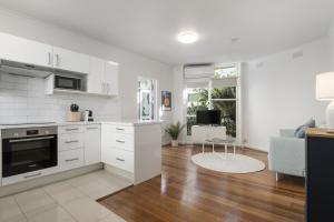 a kitchen with white cabinets and a living room at Seaside 1-Bed Stay Near Cafés & Attractions in Melbourne +6 photos