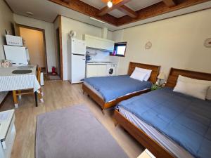 a bedroom with two beds and a desk and a kitchen at There Bengdi in Jeju