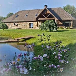 a stone house with flowers in front of a pond at Jauki Lauki in Lejasciems