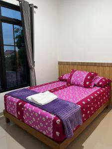 a bed with pink and purple sheets and a window at Majid's Homestay Solo in Kartosuro