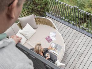 a woman sitting on a wicker chair on a balcony at Baumhaus by Hotel Gassner in Neukirchen am Großvenediger