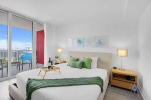 a white bedroom with a large bed and a balcony at Condo Retreat with Stunning Views and Amazing Pools in Hallandale Beach