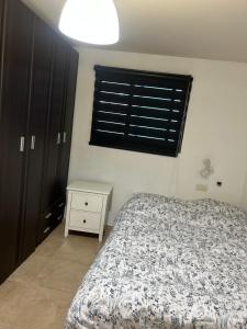 a bedroom with a bed and a nightstand and a window at דירת אירוח גלילי in Qiryat Shemona