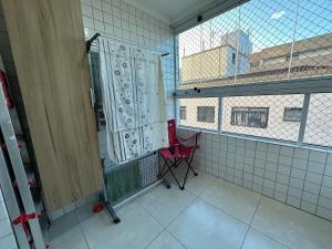 une chaise rouge dans une chambre avec fenêtre dans l'établissement Apto Alto Padrão Aviação 2Qts (1Suíte), à Praia Grande