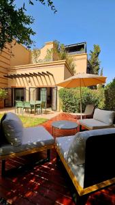 a patio with chairs and tables and an umbrella at Dar Hegoa Villa Soleil et Chaleureuse in Marrakech