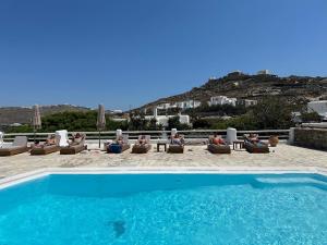 a group of people sitting in lounge chairs next to a swimming pool at Evagelia's Place in Agios Ioannis Mykonos