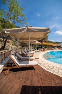 a deck with chairs and an umbrella next to a pool at Riviera Perdika Hotel in Perdika