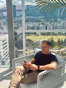 a man sitting on a bench looking at his cell phone at Luxury Apartment Leparc Residences in Quito