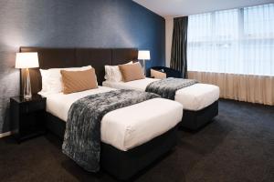 two beds in a hotel room with two lamps at Gilmer Apartment Hotel in Wellington