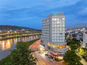 老街市Tru by Hilton Lao Cai City Riverside的一条高大的白色建筑物,毗邻一条河流