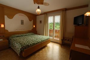 a bedroom with a bed and a television and a window at Charme Hotel Nevada in Molveno