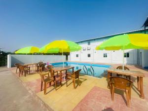 un patio con mesas y sillas con sombrillas y una piscina en Riverside Retreat Dombivli - Swimming Pool - Couple Friendly - Comfortable Stay, en Dombivli