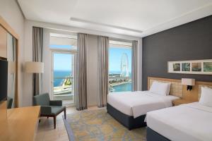 Una habitación de hotel con dos camas, un escritorio y una ventana. en DoubleTree by Hilton Dubai Jumeirah Beach, en Dubái