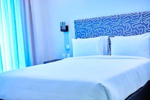 Una cama blanca en una habitación con una pared azul. en The Urban Hotel Kasama, en Kasama
