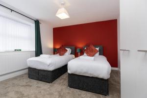 two beds in a room with a red wall at Bob Hannah Cottage in Cockfield