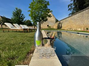 una bottiglia di vino e dei bicchieri su un tavolo accanto a una piscina di La Ferme du Château de Grisy, Piscine, 10p a Vendeuvre