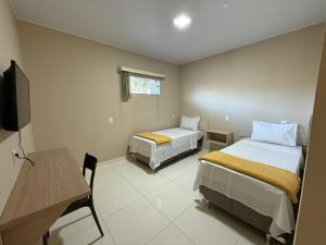 a room with two beds and a desk and a television at Pousada Itajuipe II in Vitória da Conquista