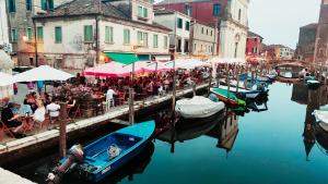 a group of people sitting at tables near a canal with boats at Coramino in Chioggia