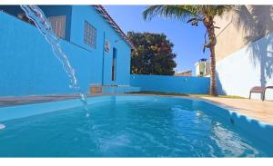 a swimming pool with a fountain in front of a blue house at Casa Encanto da Vila in Saquarema