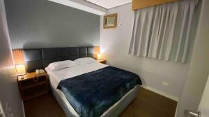 a bedroom with a bed with a blue blanket on it at Flat confortável com recepção 24h e vaga de garagem in São Paulo