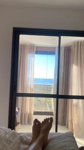 personas con pies sobre una cama frente a una ventana en NOVO frente ao Mar - 750m da Orla e Pq dos Ventos - Oceanfront - 3 Guests, en Salvador