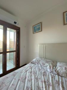 a white bedroom with a bed and a window at Duplex Acolhedor - Duas quadras do Mar Centro in Tramandaí