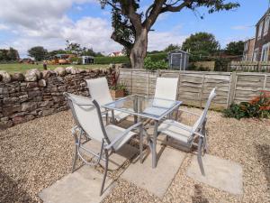 a glass table with three white chairs and a fence at Lavender Cottage in Chathill