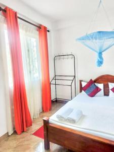 a bedroom with a bed with orange curtains and a window at La Belle Homestay in Kandy