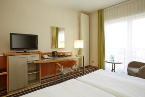 ヒュルトにあるH+ ホテル ケルン ヒュルトのベッド、デスク、テレビが備わるホテルルームです。